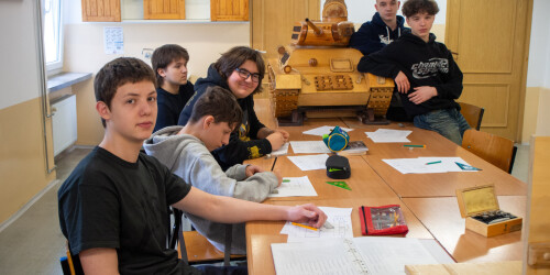 Uczniowie siedzą przy stole z zeszytami w pracowni technologii drewna