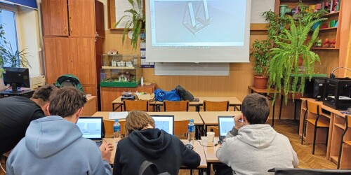 Uczniowie siedzą tyłem do obiektywu i pracują przy laptopach nad projektem wydruku 3D